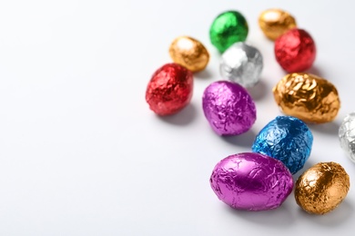 Chocolate eggs wrapped in colorful foil on white background. Space for text