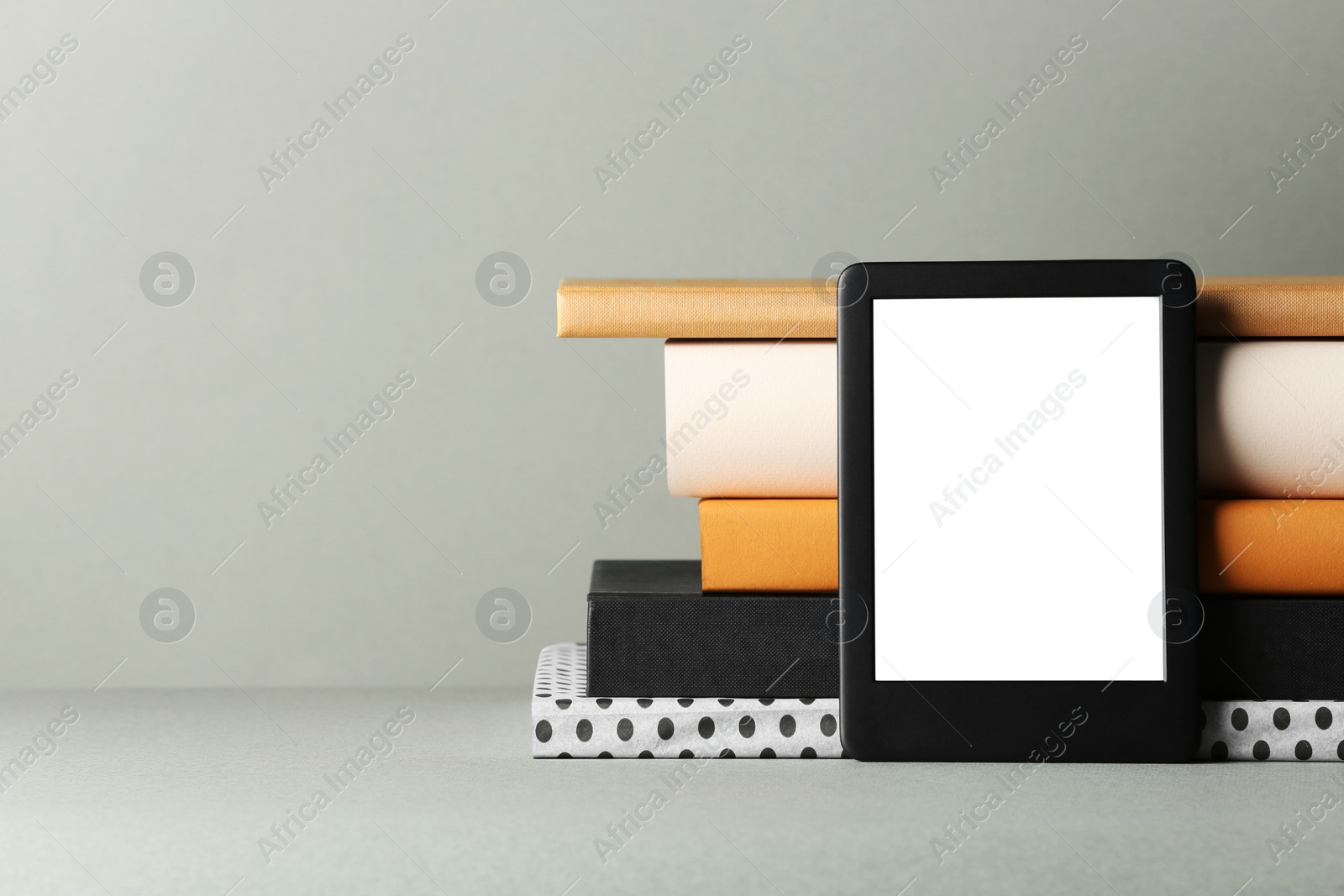 Photo of Modern e-book reader and stack of hard cover books on light grey table. Space for text