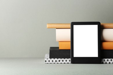 Modern e-book reader and stack of hard cover books on light grey table. Space for text