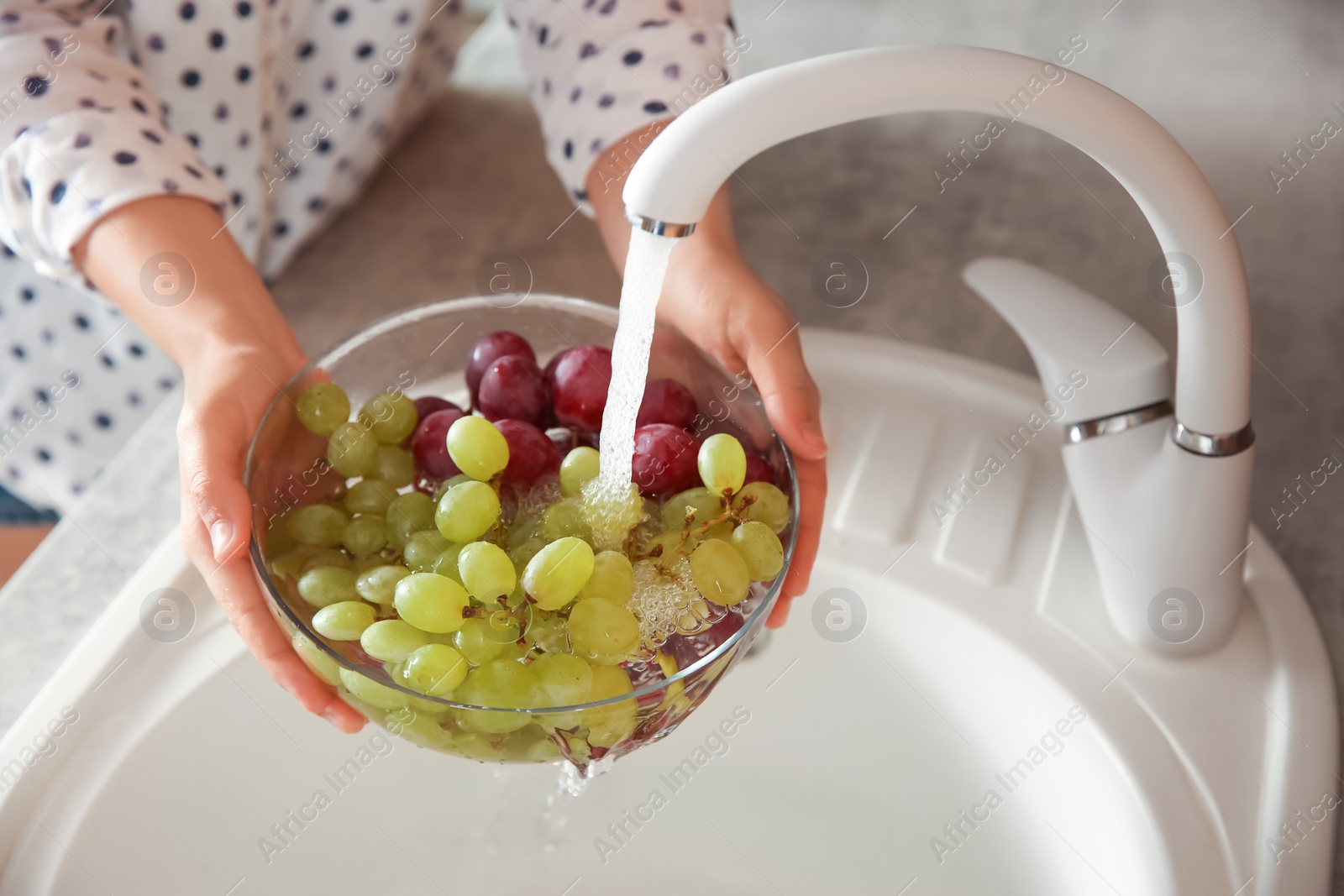 Photo of Woman washing fresh grapes in kitchen sink, closeup