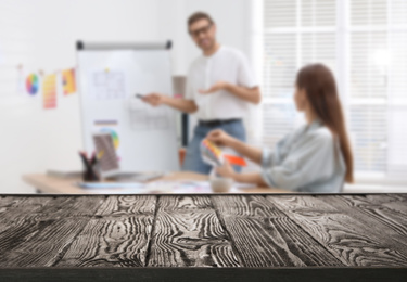 Empty wooden surface and blurred view of professional interior designers working in office, closeup. Space for text 