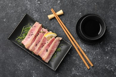 Photo of Pieces of delicious tuna steak served on black table, flat lay