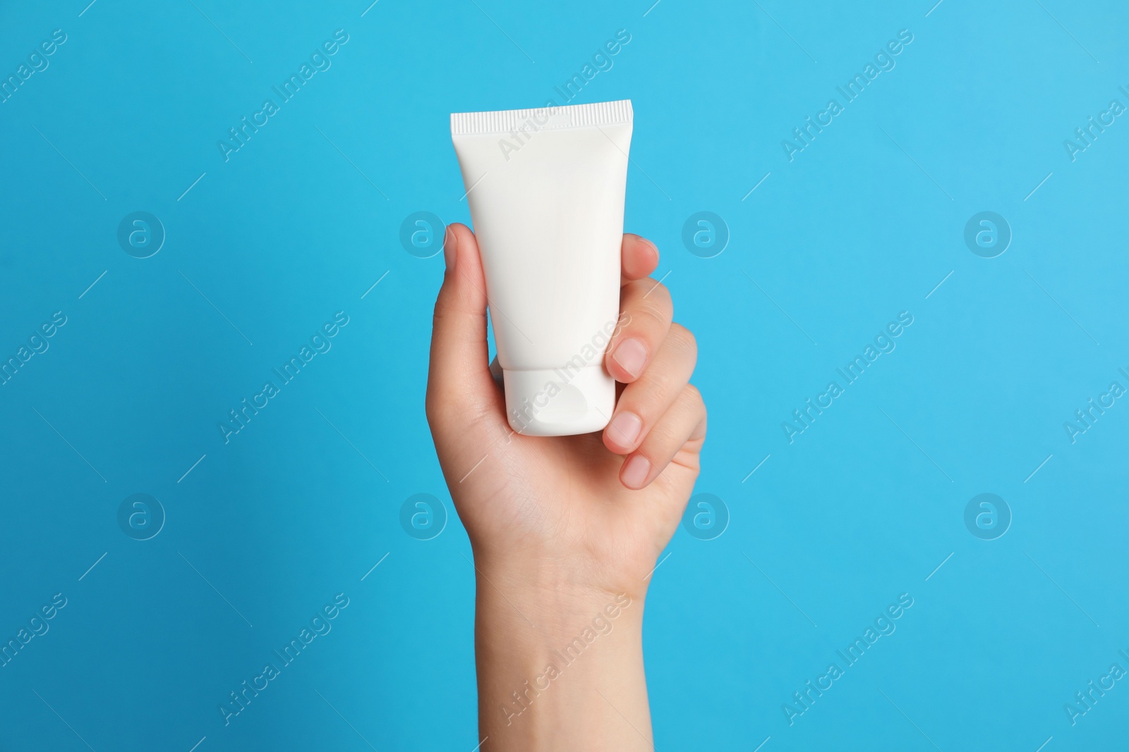 Photo of Woman holding tube of face cream on light blue background, closeup