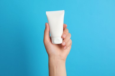 Photo of Woman holding tube of face cream on light blue background, closeup