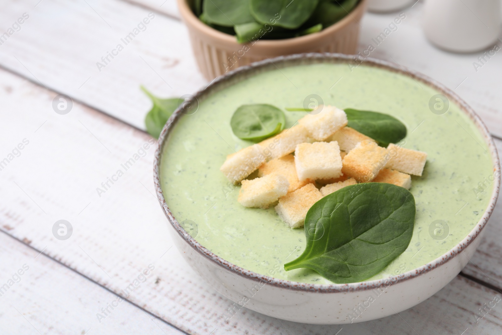 Photo of Delicious spinach cream soup with leaves and croutons in bowl on white wooden table, space for text