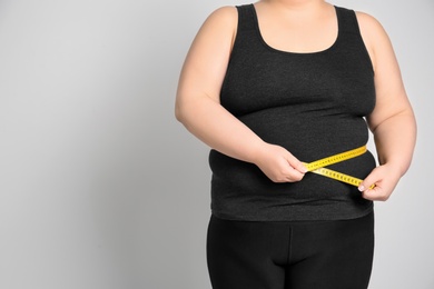 Photo of Overweight woman with measuring tape on light background