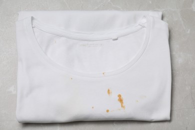 Photo of Dirty t-shirt with stains of sauce on light grey marble table, top view