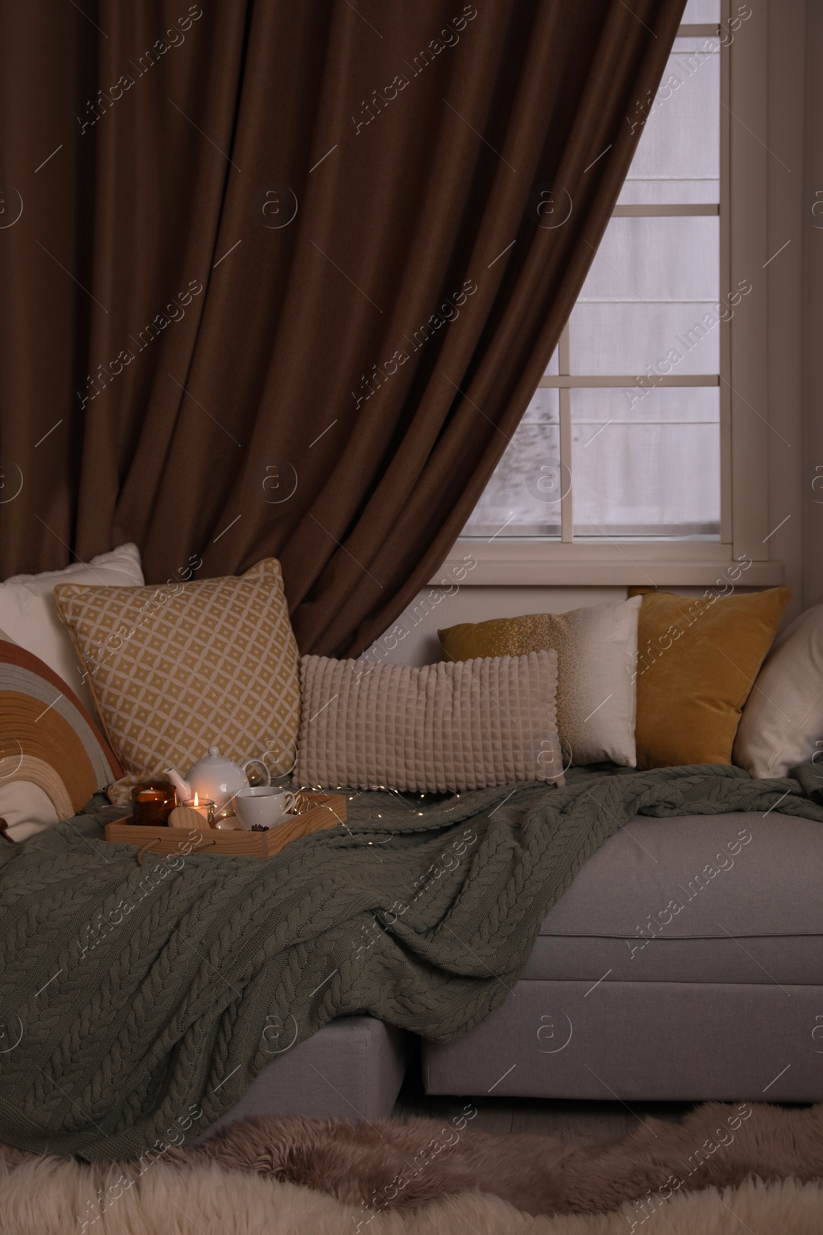 Photo of Comfortable lounge area with knitted blanket and soft pillows near window in room