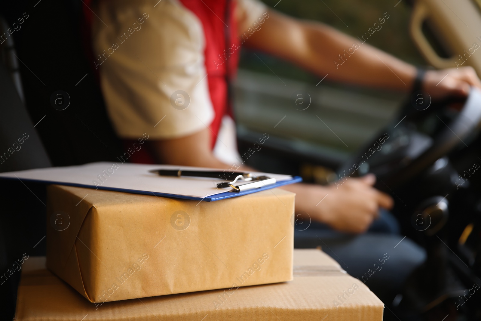 Photo of Courier driving delivery van, focus on parcels and clipboard