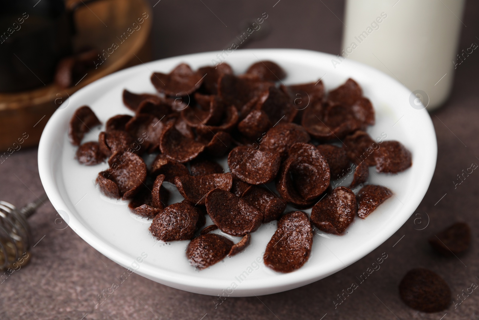 Photo of Breakfast cereal. Chocolate corn flakes and milk in bowl on brown table, closeup