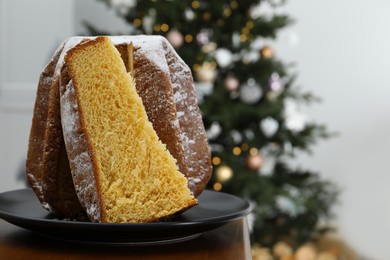 Photo of Delicious Pandoro cake decorated with powdered sugar near Christmas tree in room, space for text. Traditional Italian pastry