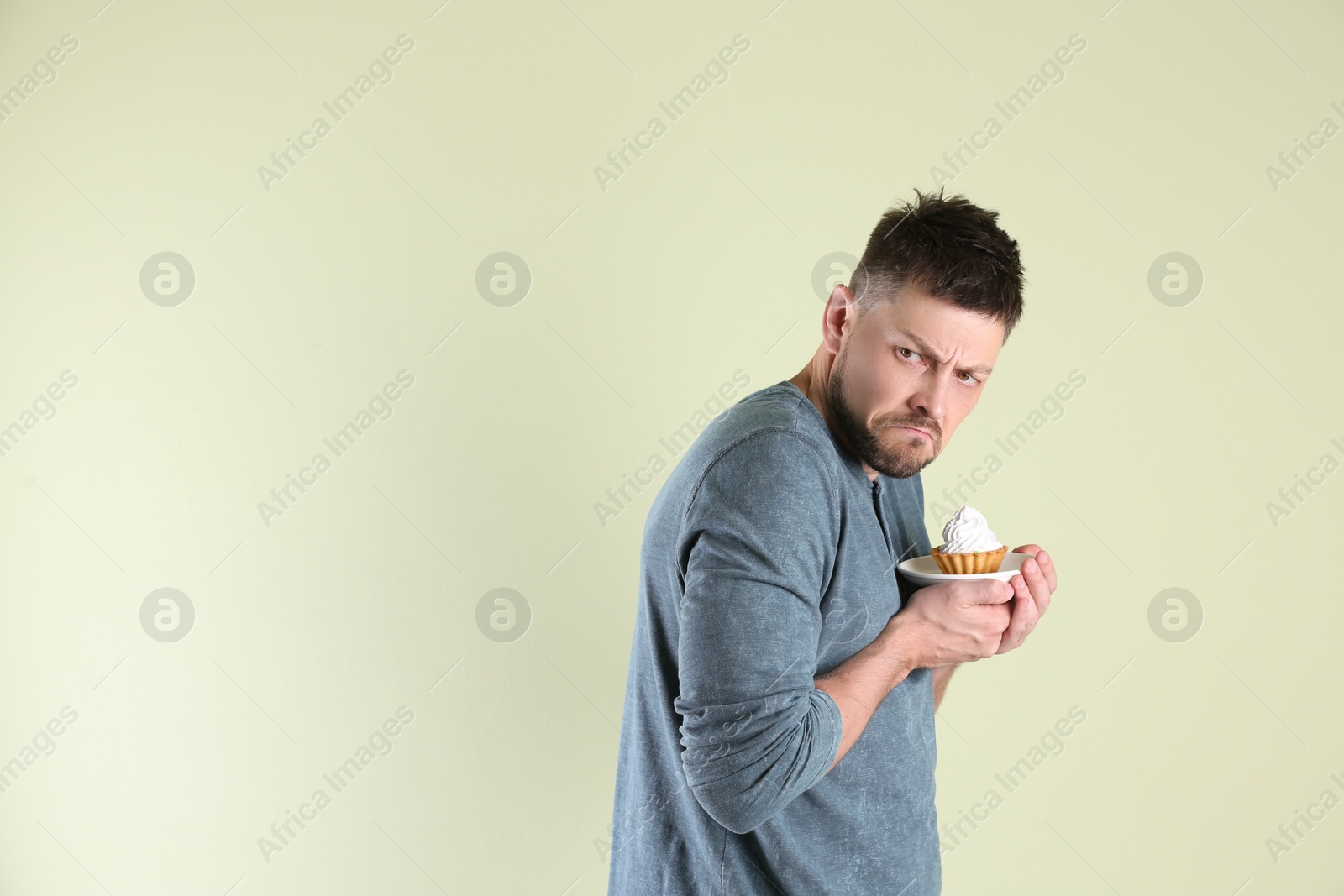 Photo of Greedy man hiding cupcake on light background, space for text