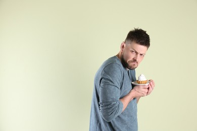 Greedy man hiding cupcake on light background, space for text