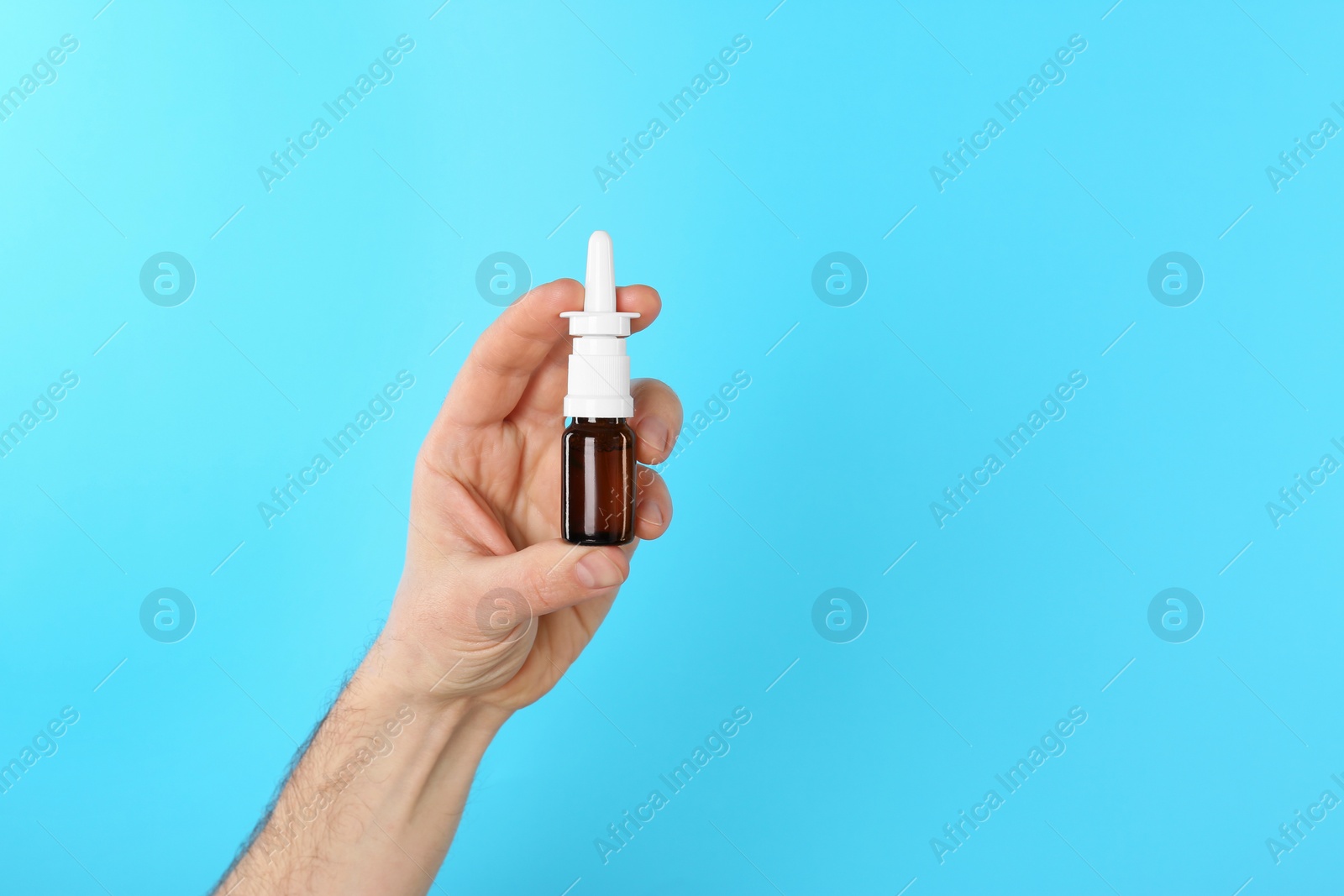 Photo of Man holding nasal spray on light blue background, closeup. Space for text