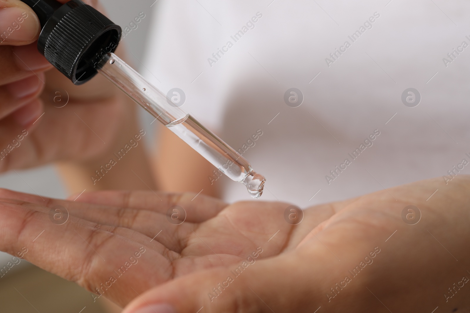 Photo of Woman applying cosmetic serum onto her hand, closeup