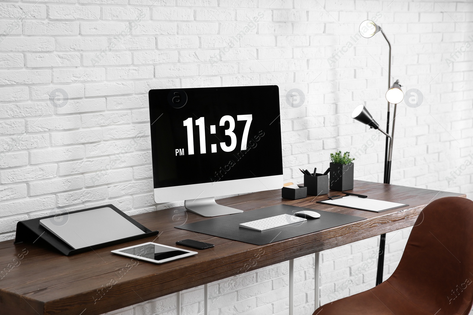 Photo of Modern workplace interior with computer and devices on table near brick wall