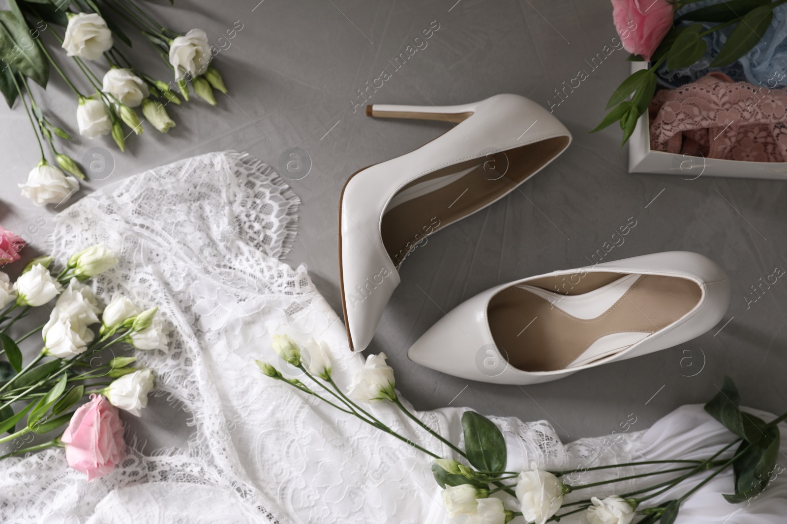 Photo of Flat lay composition with wedding dress, white high heel shoes and flowers on grey background