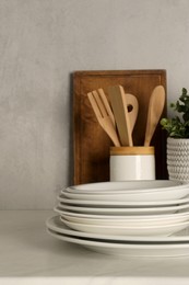 Set of clean plates and different kitchen utensils on light table near wall