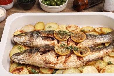 Photo of Baking tray with delicious baked sea bass fish and potatoes on table, closeup