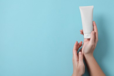 Photo of Woman with tube of hand cream on light blue background, top view. Space for text