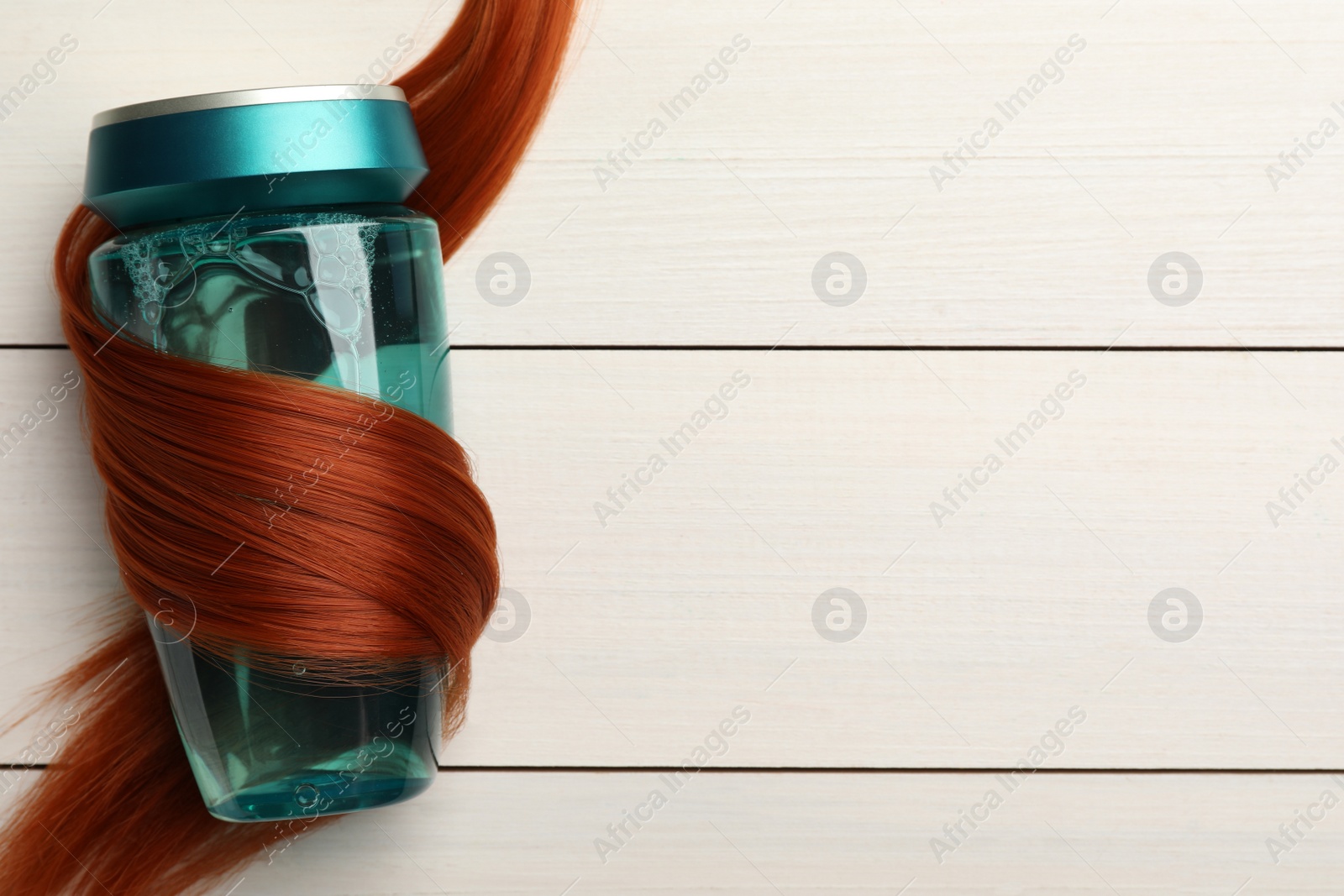 Photo of Bottle wrapped in lock of hair on white wooden background, top view with space for text. Natural cosmetic product