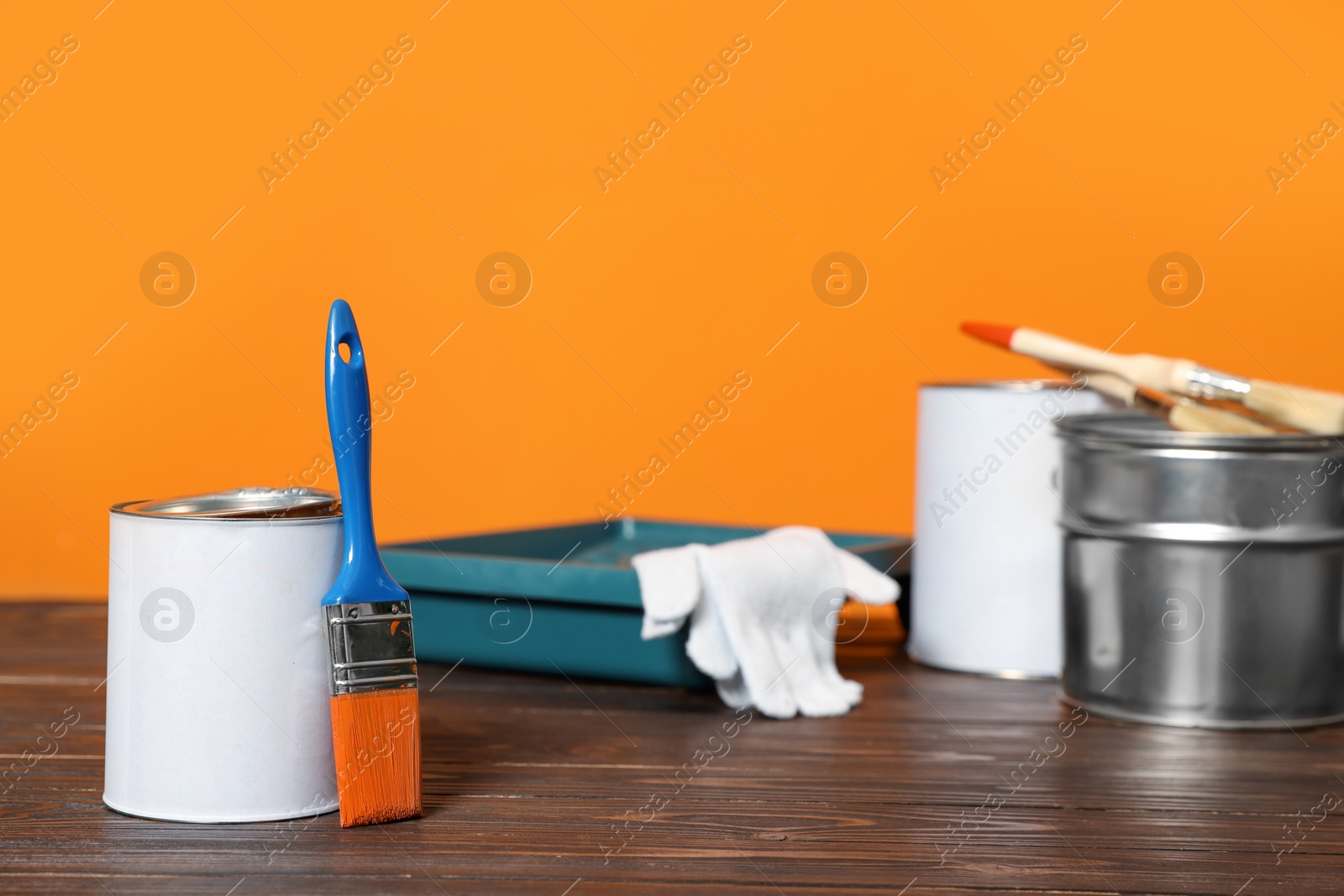 Photo of Can with paint, brush and renovation equipment on wooden table against orange background