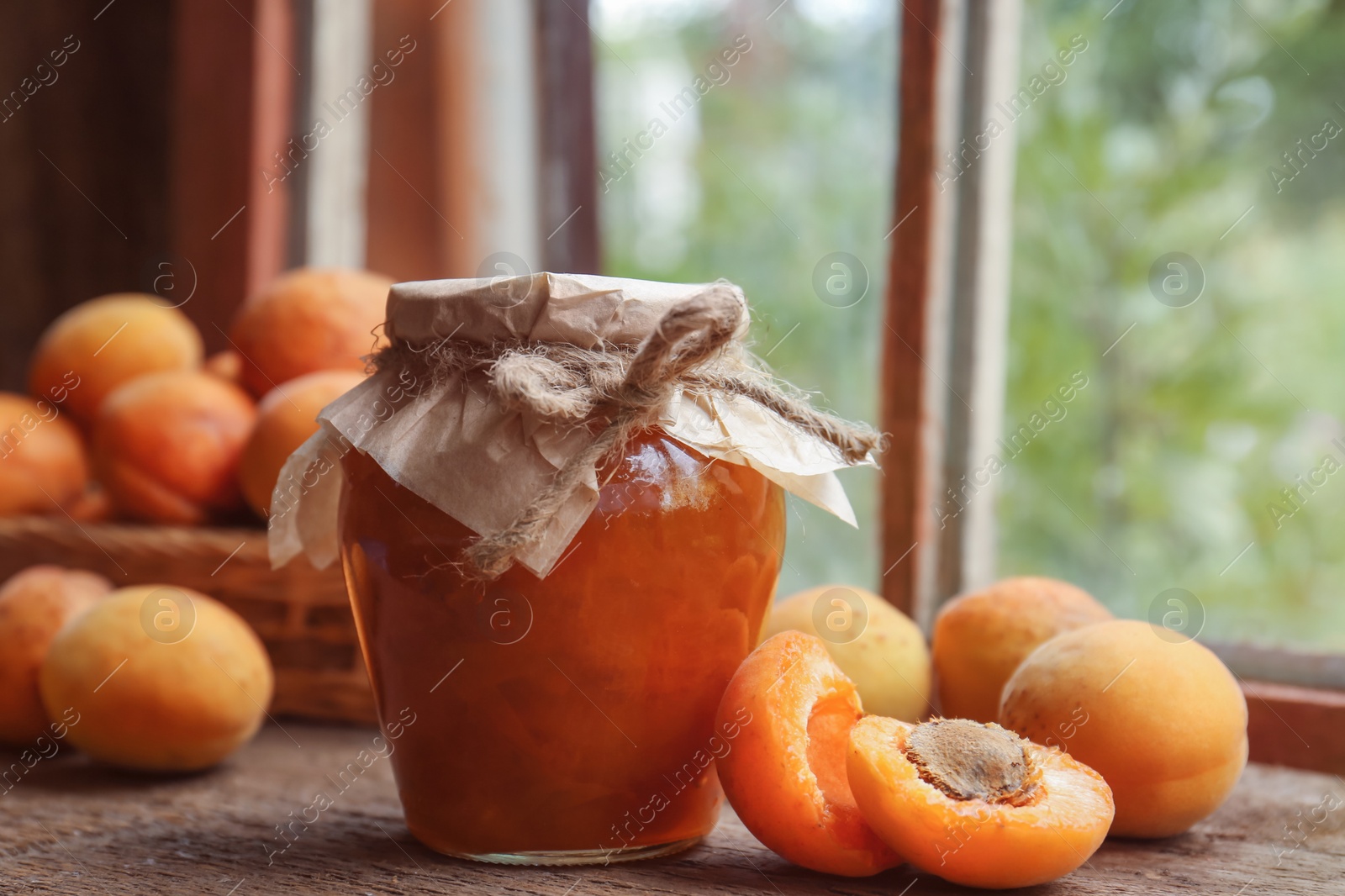 Photo of Jar of delicious jam and fresh ripe apricots on wooden table indoors. Fruit preserve