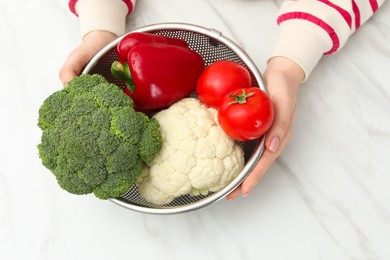 Photo of Woman holding colander with fresh vegetables at white marble table, closeup