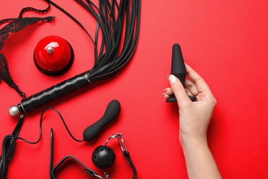 Photo of Young woman holding anal plug near sex toys on red background, top view