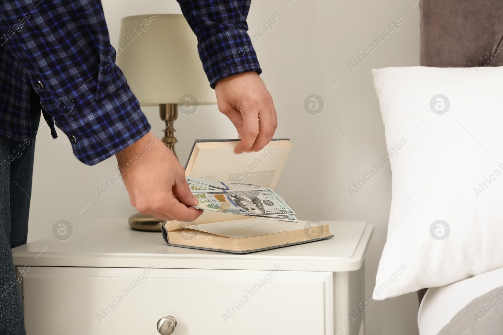 Photo of Man hiding dollar banknotes in book indoors, closeup. Money savings