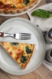 Photo of Piece of delicious homemade salmon quiche with broccoli and fork on wooden table, flat lay