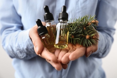 Photo of Woman holding bottles of essential oils and fir branches, closeup