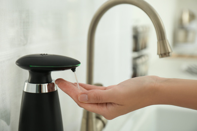 Photo of Woman using automatic soap dispenser in kitchen, closeup