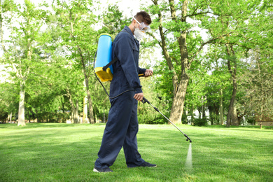 Photo of Worker spraying pesticide onto green lawn outdoors. Pest control