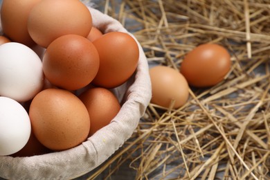Photo of Fresh chicken eggs in bowl and dried straw on table, closeup. Space for text