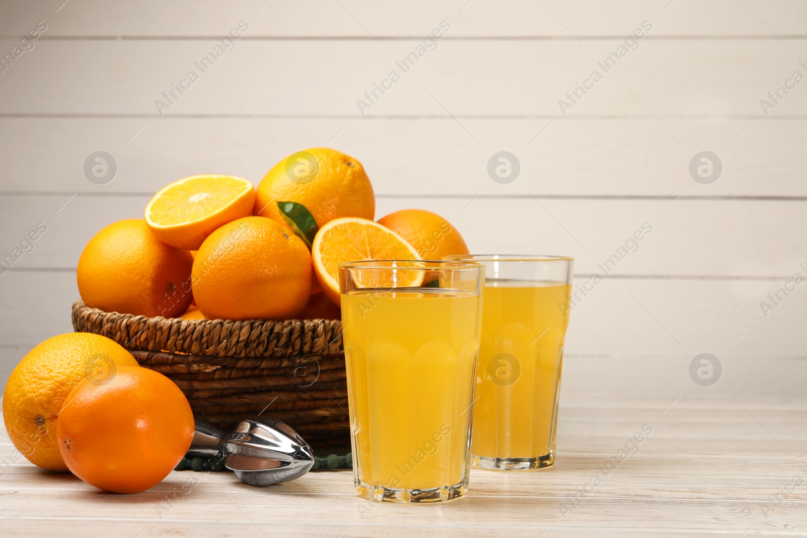 Photo of Many ripe juicy oranges, squeezer and fresh juice on white wooden table. Space for text