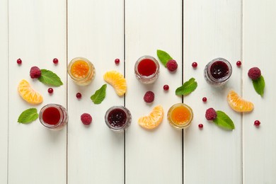 Jars of different jams and fresh ingredients on white wooden table, flat lay