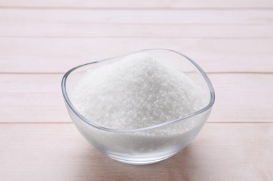 Photo of Granulated white sugar in bowl on wooden table, closeup
