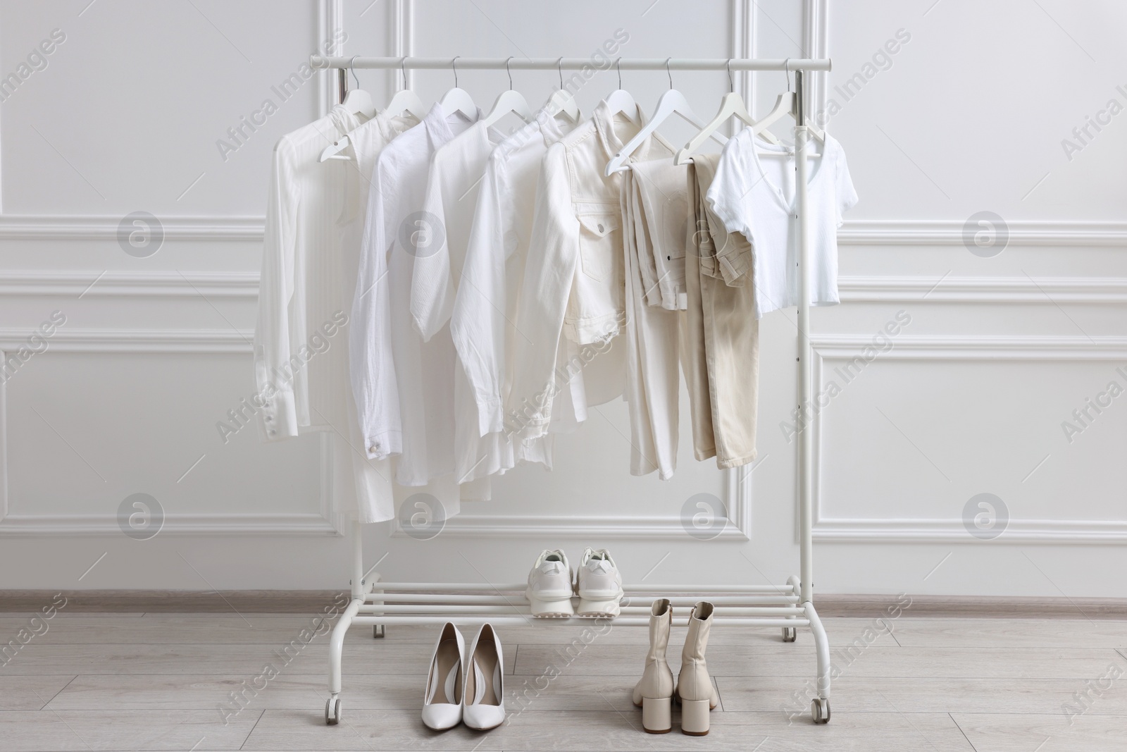 Photo of Rack with different stylish women`s clothes and shoes near white wall indoors