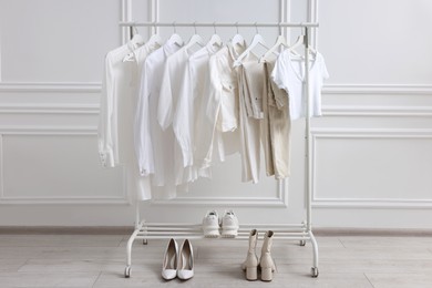 Rack with different stylish women`s clothes and shoes near white wall indoors