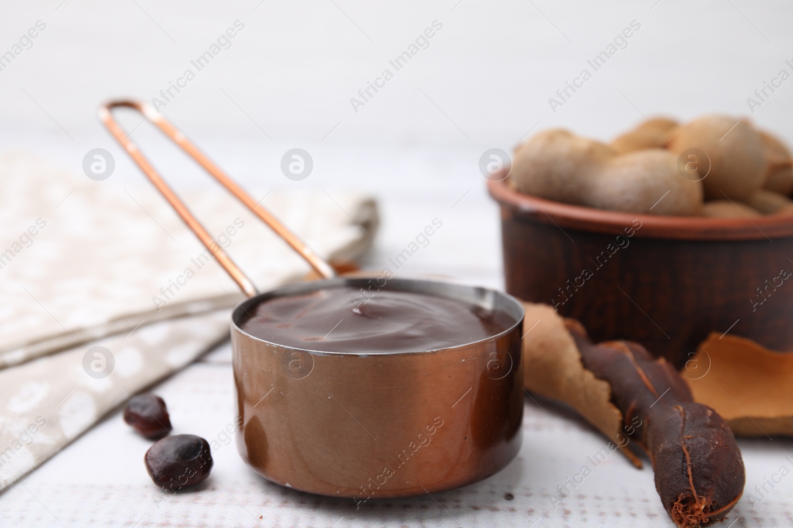 Measuring cup with tasty tamarind sauce and fresh pods on white wooden table Photo of Measuring cup with tasty tamarind sauce and fresh pods on white wooden table