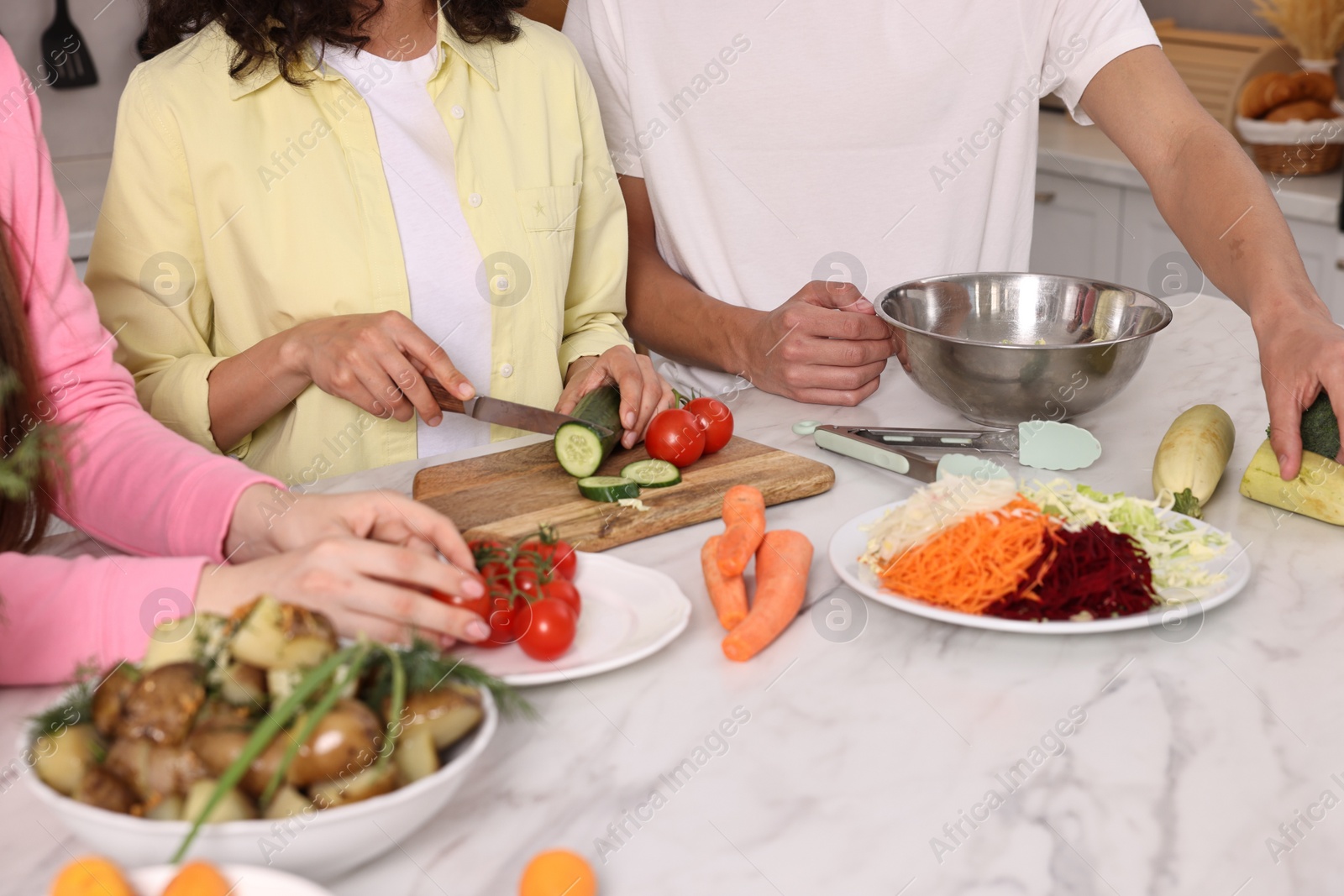 Photo of Friends cooking healthy vegetarian meal at white marble table in kitchen, closeup