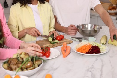 Friends cooking healthy vegetarian meal at white marble table in kitchen, closeup