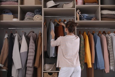 Photo of Young woman choosing clothes in wardrobe closet, back view