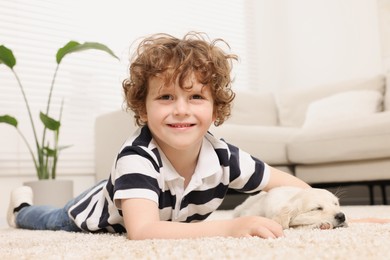 Photo of Little boy with cute puppy on beige carpet at home