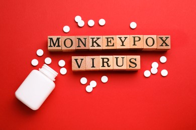 Photo of Words Monkeypox Virus made of wooden cubes and pills on red background, flat lay