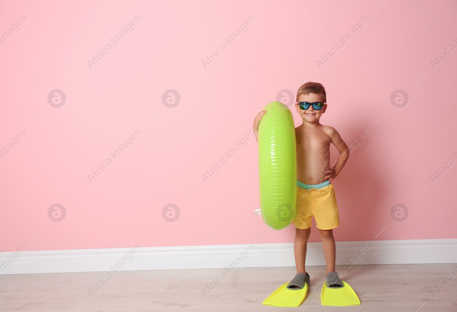 Photo of Cute little boy with inflatable ring wearing flippers near color wall