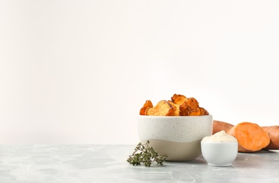 Bowl of sweet potato chips with sauce and herbs on table against white background. Space for text