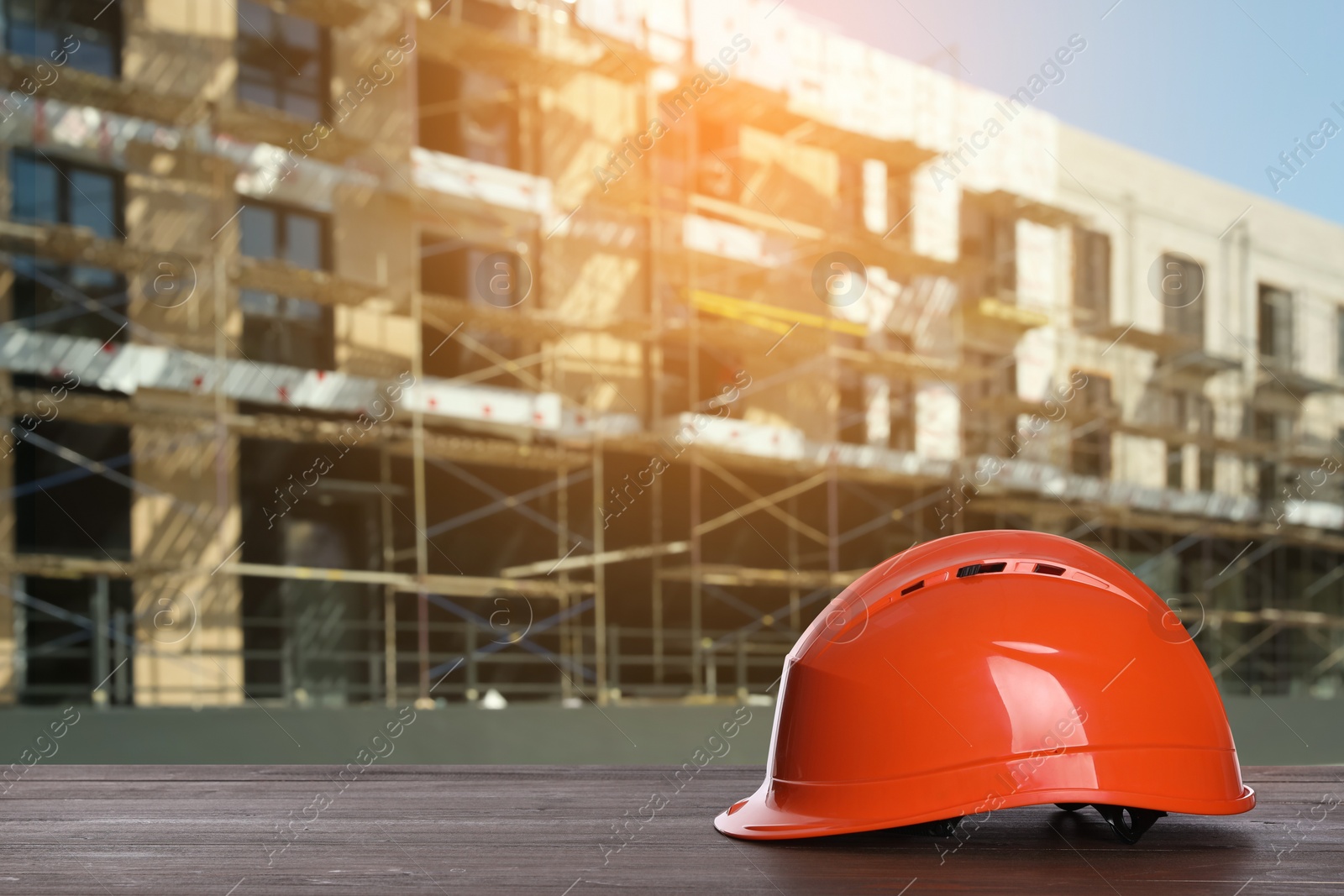 Image of Safety equipment. Hard hat on wooden surface near unfinished building outdoors, space for text