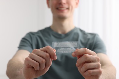 Photo of Young man with whitening strips on light background, closeup